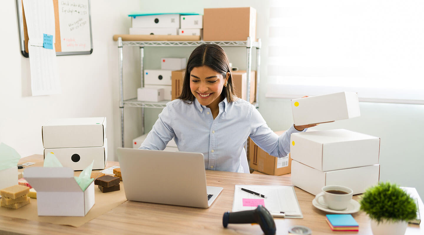 Woman sitting in front of desk, smiling and arranging white box packages